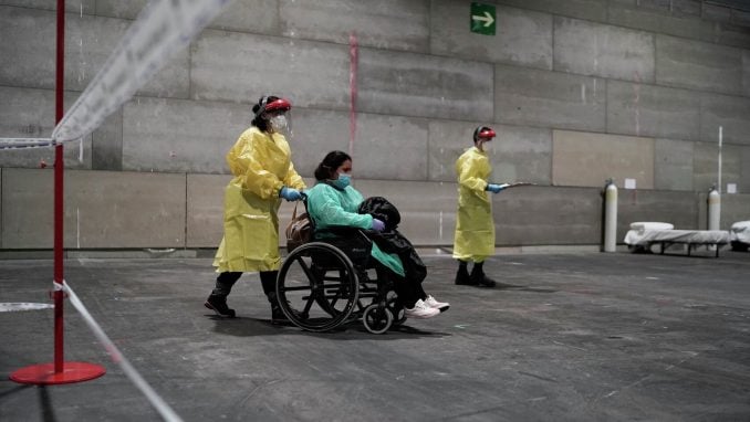 Eine Krankenschwester schiebe eine Corona-Patientin in einem Rollstuhl durch eine Halle