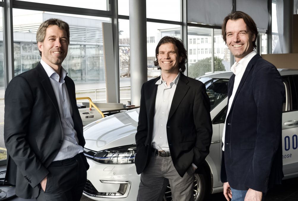 Three forty-something men in suit jackets standing in front of a car smiling
